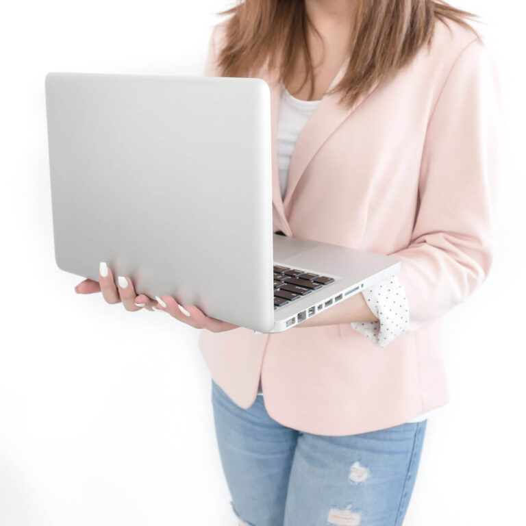 Woman holding laptop in light pink blazer.