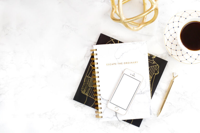 Notebook, phone, pen, and coffee on marble background.