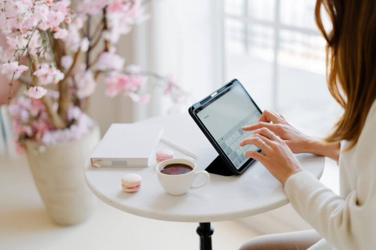 Woman typing on tablet near flowers and coffee