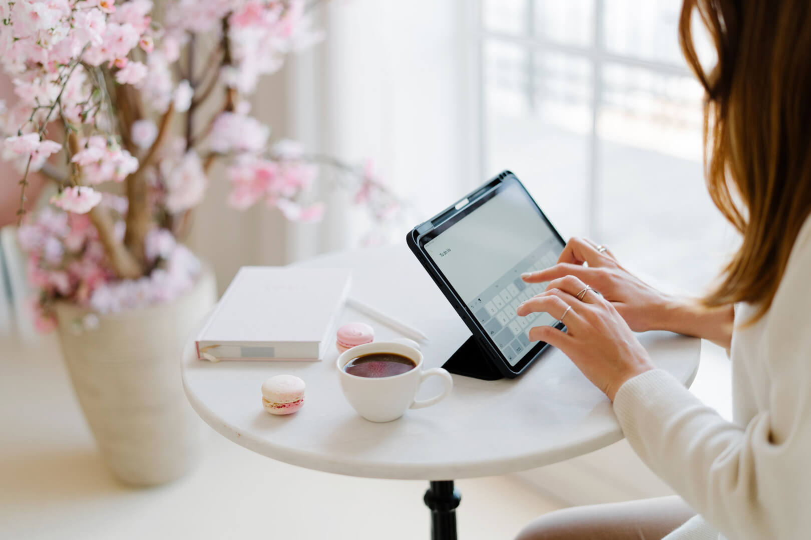 Woman typing on tablet near flowers and coffee