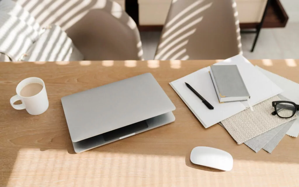 Minimalist desk with laptop, notebook, coffee, glasses.