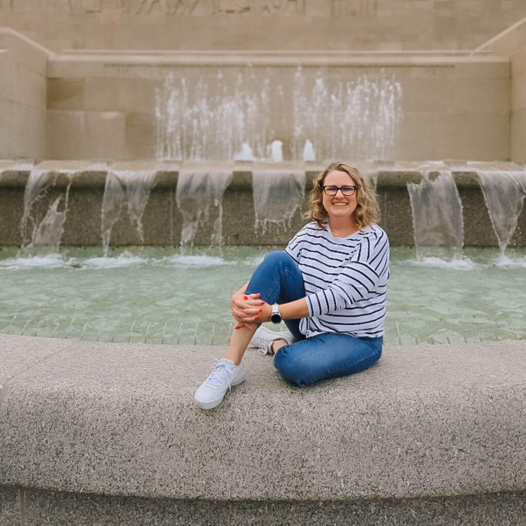 Woman sitting by fountain, smiling at camera