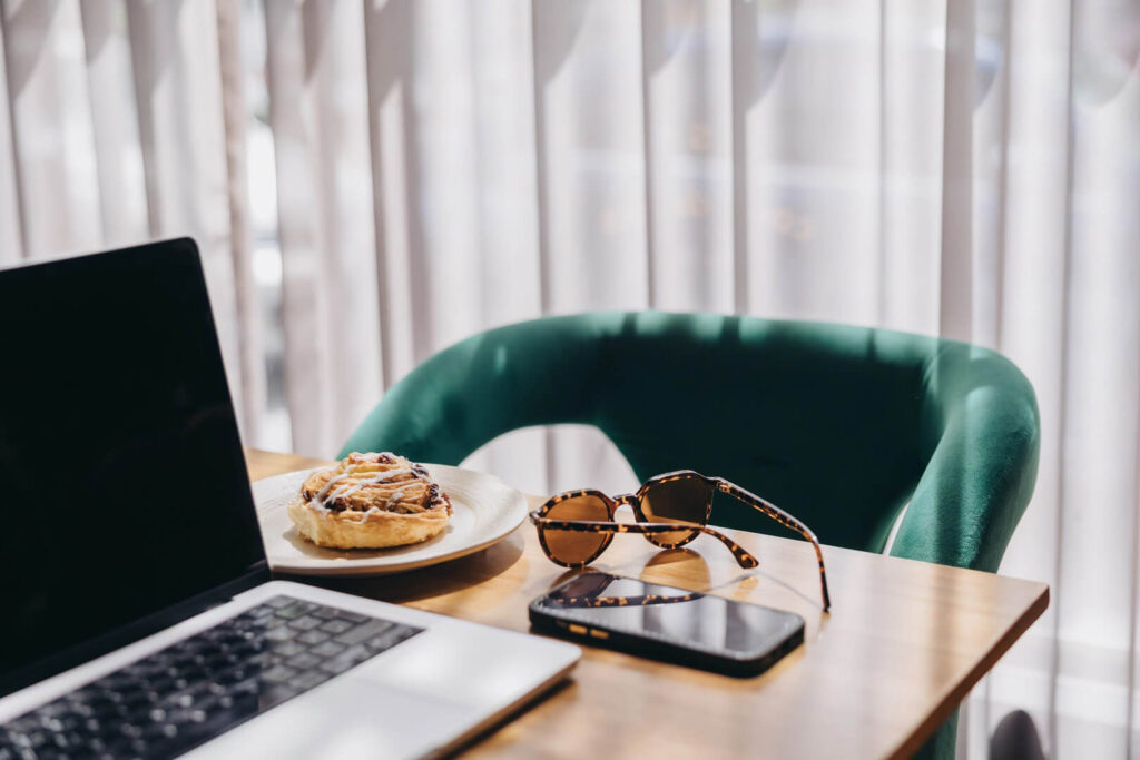 Laptop, pastry, sunglasses, and phone on table