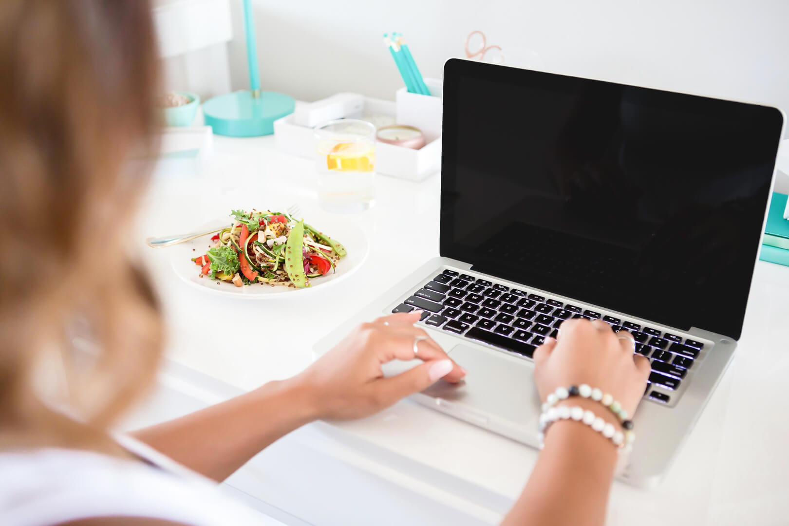 Person typing on laptop beside fresh salad