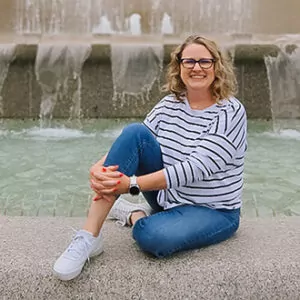 Woman sitting by fountain, smiling at camera