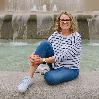 Woman sitting by fountain, smiling at camera