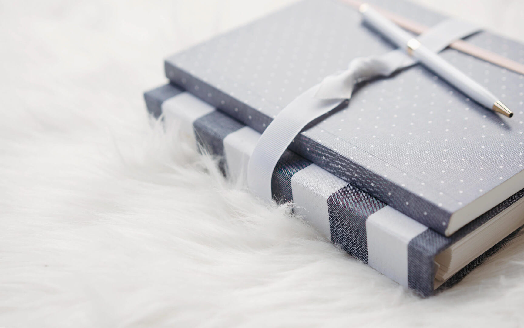 Gray polka-dot notebooks with pen and ribbon on white fur