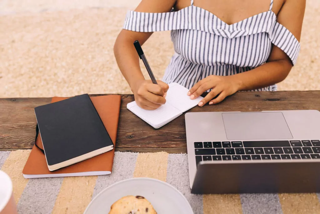 Woman writing in notebook beside laptop outdoors