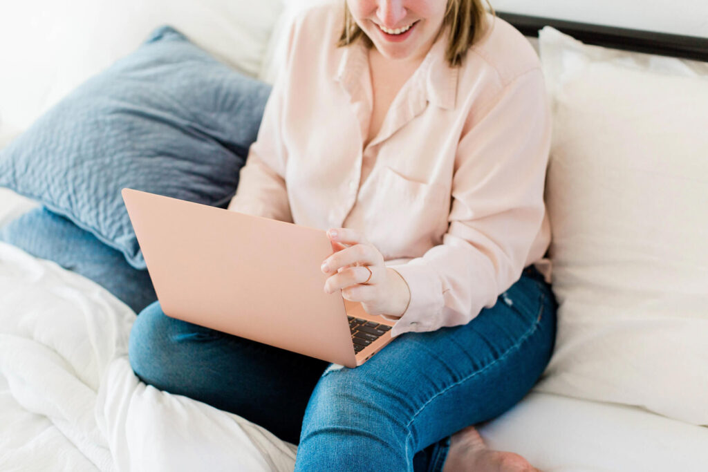 Smiling woman using laptop while sitting on bed